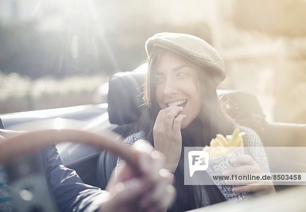 Young couple in convertible  woman eating chips
