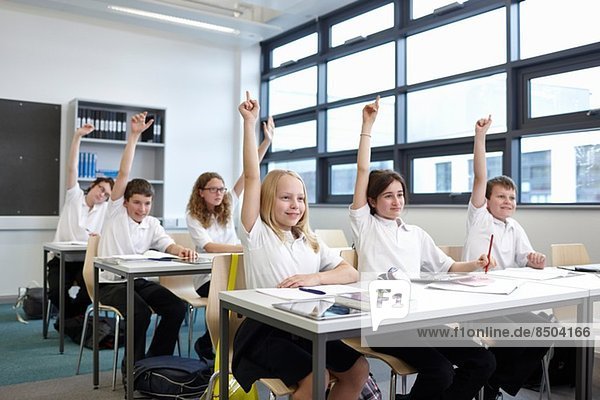 Group of schoolchildren with hands raised in classroom