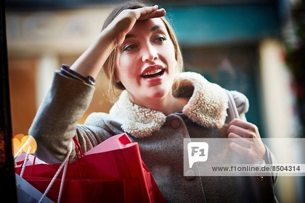 Junge Frau mit Einkaufstasche  Blick durchs Fenster