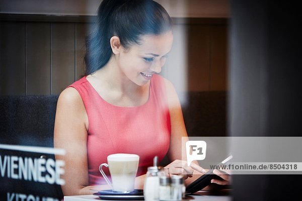 Junge Frau sitzend im Café mit digitalem Tablett und heißem Getränk