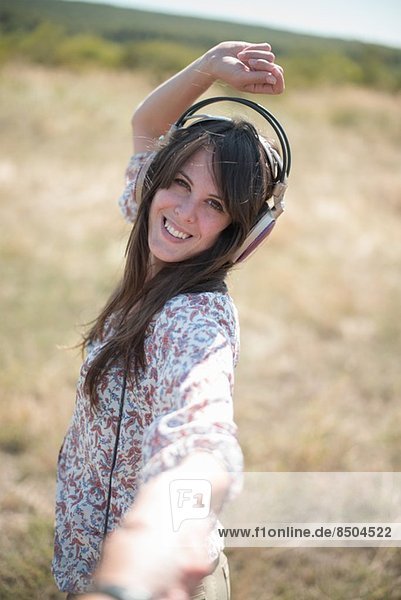 Portrait of mid adult woman dancing in field with arms raised  wearing headphones