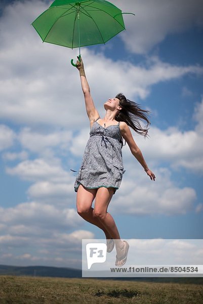 Mid adult woman holding green umbrella  jumping