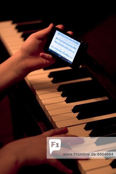Nahaufnahme der Hände mit dem Smartphone während des Klavierspiels