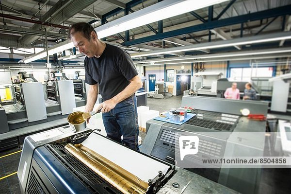 Arbeiter beim Auftragen von Goldfarbe auf die Druckmaschine in der Druckerei