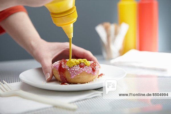 Woman squirting donut with ketchup and mustard