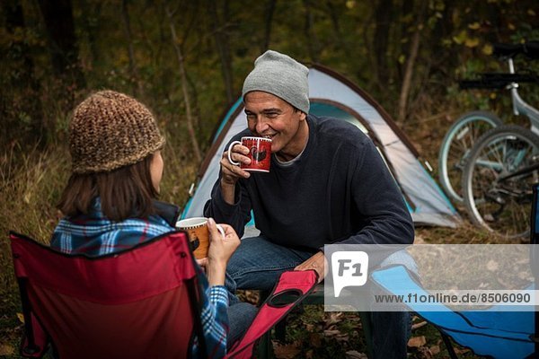 Reife Paare sitzen auf Campingstühlen vor dem Zelt und trinken heiße Getränke.