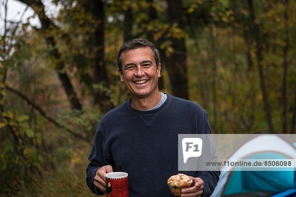 Mature man in forest holding cupcake and hot drink