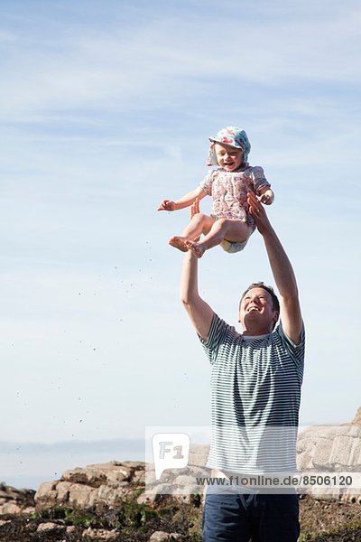 Vater wirft Kind in die Luft am Strand