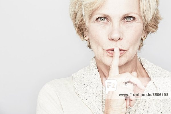 Abgeschnittenes Studioporträt einer älteren Frau mit Finger auf den Lippen
