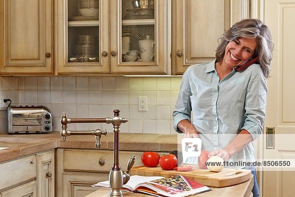 Reife Frau mit dem Handy und der Zubereitung von Speisen in der Küche