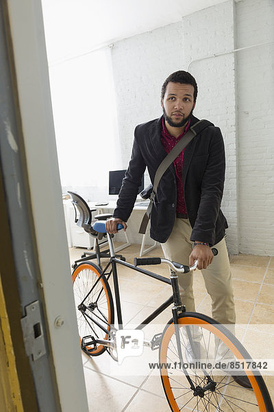 Mixed race businessman wheeling bicycle in office