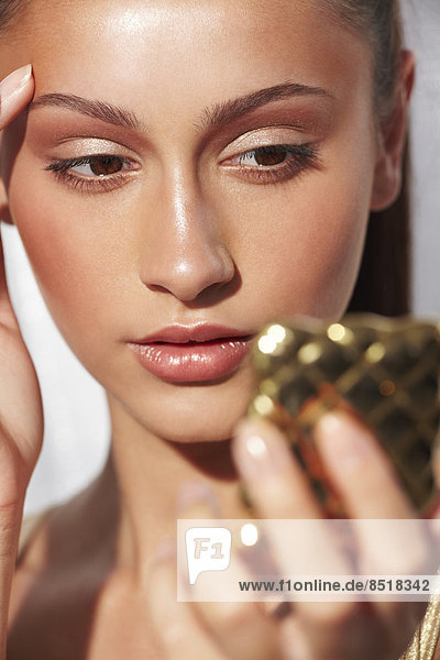 Close-up of glamorous young woman with glowing skin holding a compact mirror
