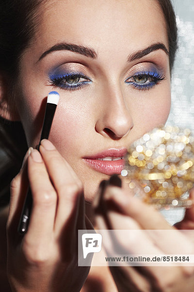 Close-up of beautiful young woman applying blue eyeshadow
