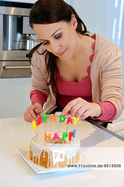 Eine junge Frau dekoriert einen Geburtstagskuchen mit Kerzen.