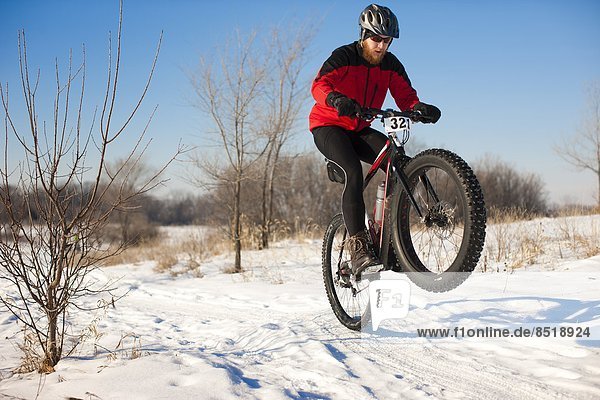 A fat tire biker pops a wheely in the snowy terrain.