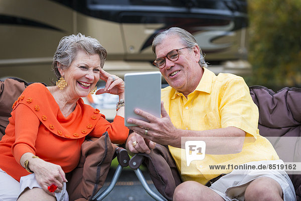 USA  Texas  Senior couple in front of their recreational ßehicle using mini tablet pc