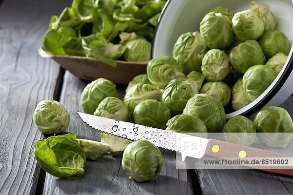 Bowl of Brussels sprouts  plate with peels and kitchen knife on grey wooden table