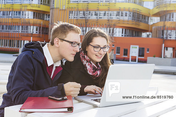 Two students using laptop outdoors
