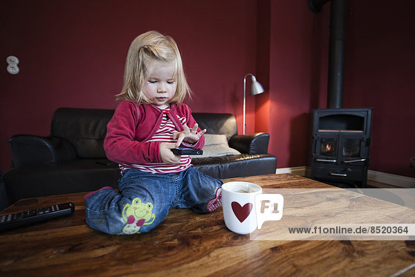 Little girl sitting on wooden table  testing smart phone