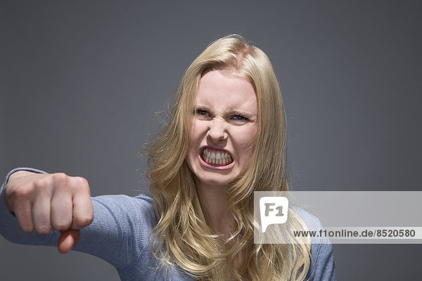 Porträt einer wütenden jungen Frau mit ausgestreckter Faust und entblößten Zähnen