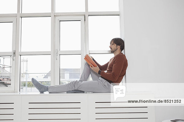 Mann liest Buch  sitzt auf Fensterbank
