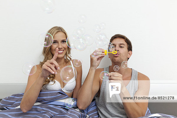 Junges Paar im Bett sitzend  Seifenblasen blasend