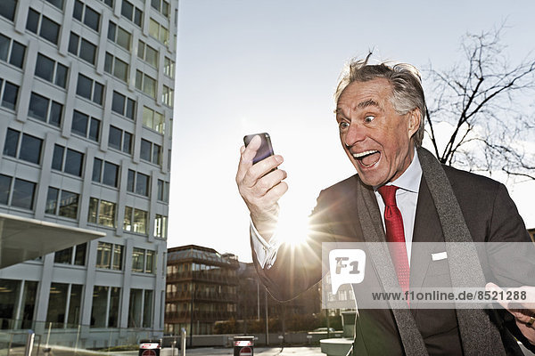 Senior Geschäftsmann schaut auf sein Smartphone und flippt aus.