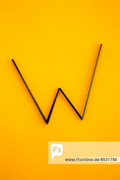 'Letter ''W'' formed of nails and threads at yellow background  studio shot'
