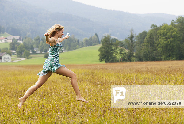 Austria  Salzkammergut  Mondsee  young woman jumping in a meadow
