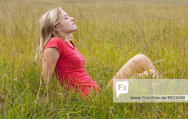 Austria  Salzkammergut  Mondsee  young woman sitting in a meadow