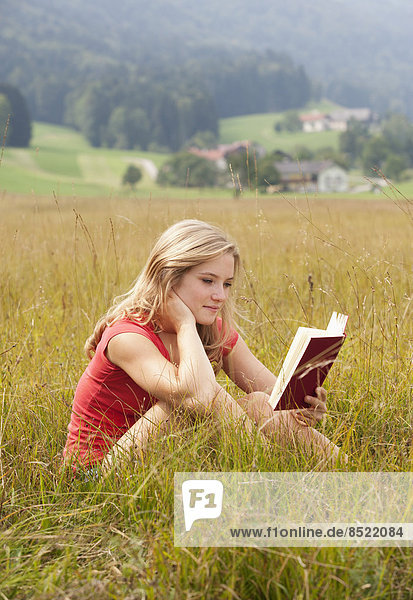 Österreich  Salzkammergut  Mondsee  junge Frau liest Buch auf einer Wiese
