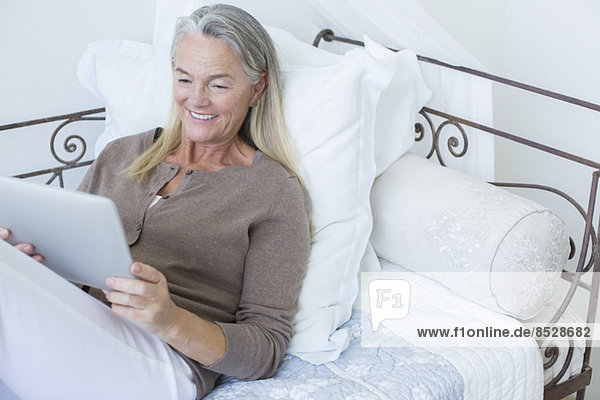 Seniorin mit digitalem Tablett auf dem Bett