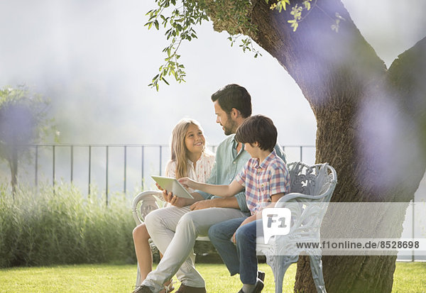 Vater und Kinder mit digitalem Tablett auf der Bank im Park