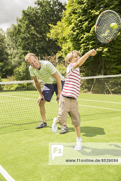 Father and son playing tennis on grass court