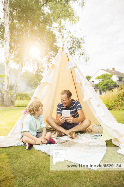 Father and son using digital tablet in teepee in backyard