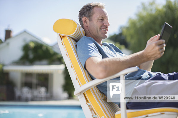 Mann liest im Sessel am Pool