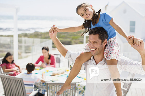 Vater trägt Tochter auf Schultern auf sonniger Terrasse