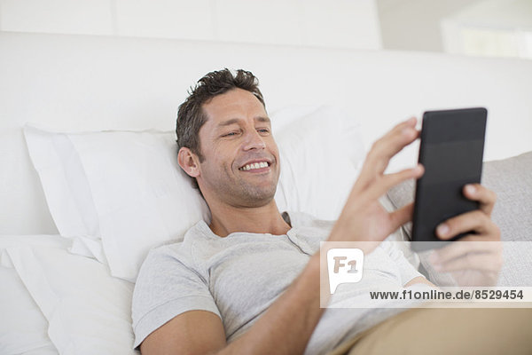 Mann mit digitalem Tablett im Bett