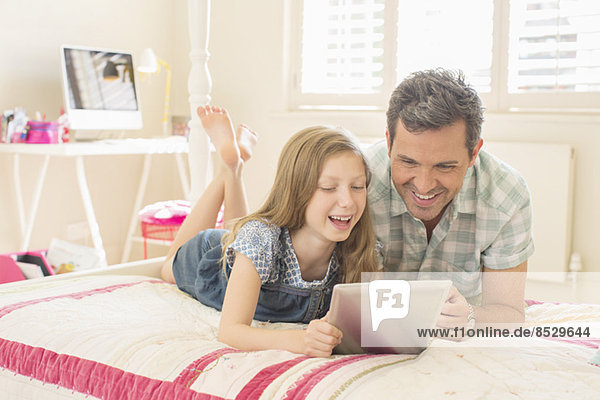 Vater und Tochter mit digitalem Tablett auf dem Bett