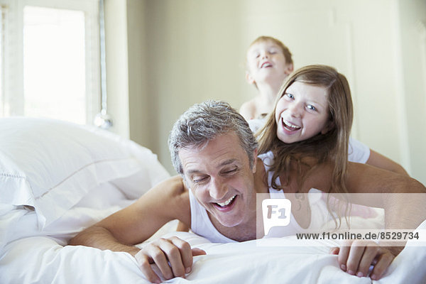 Vater und Kinder spielen auf dem Bett