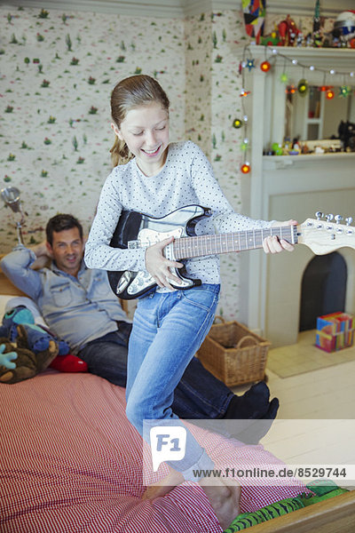 Mädchen spielt Gitarre für Vater im Schlafzimmer