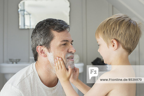 Junge reibt Rasierschaum auf Vaters Gesicht