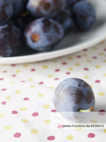 A plum in front of a plate of plums