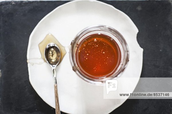 Honigglas und Löffel auf Teller