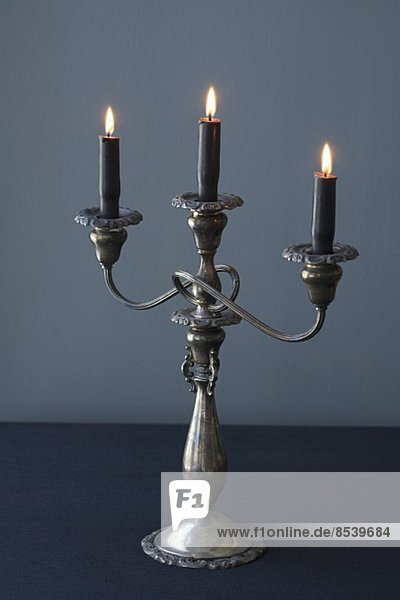 Dreiarmiger Kerzenleuchter mit schwarzen brennenden Kerzen