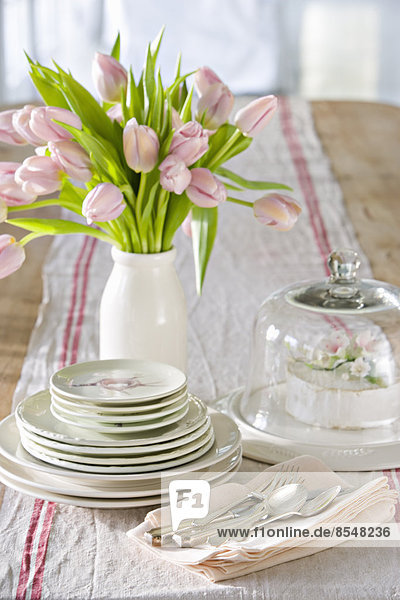 A table laid for a meal with a vase of pink tulips.
