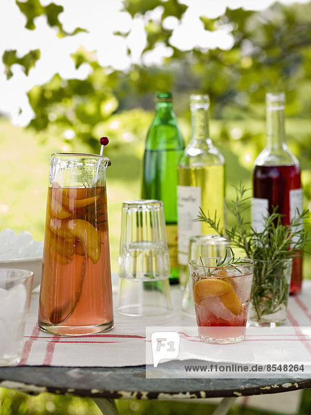 Ein in einem Garten aufgestellter Buffettisch für ein Essen im Freien. Getränke  Flaschen  ein Krug mit Punsch und Gläser.
