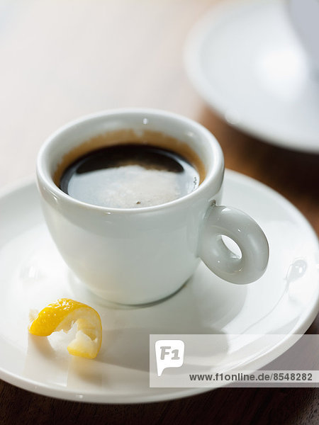 Eine Tasse schwarzer Kaffee in einer Tasse aus weißem Porzellan mit einer kleinen Drehung Zitronenschale in der Untertasse.