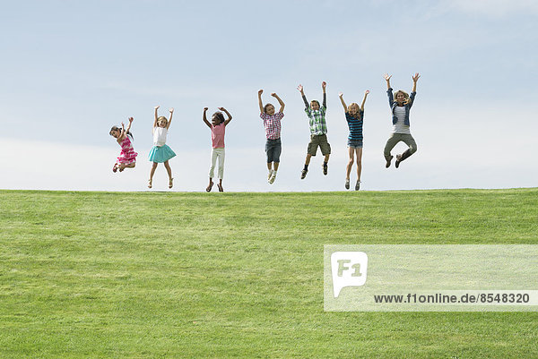 Eine Gruppe von Kindern auf dem Gipfel eines Hügels  die in einer Reihe in die Luft springen.