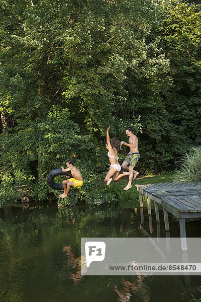 Drei kleine Jungen springen vom Steg in ein stilles Wasserbecken.